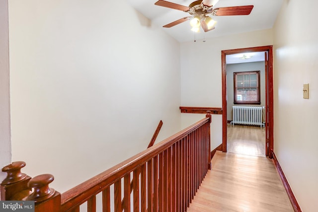 hallway featuring baseboards, light wood-style flooring, an upstairs landing, and radiator