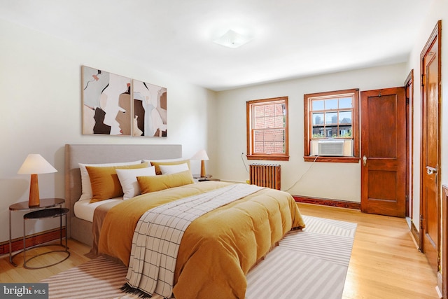 bedroom with light wood finished floors, radiator heating unit, and cooling unit