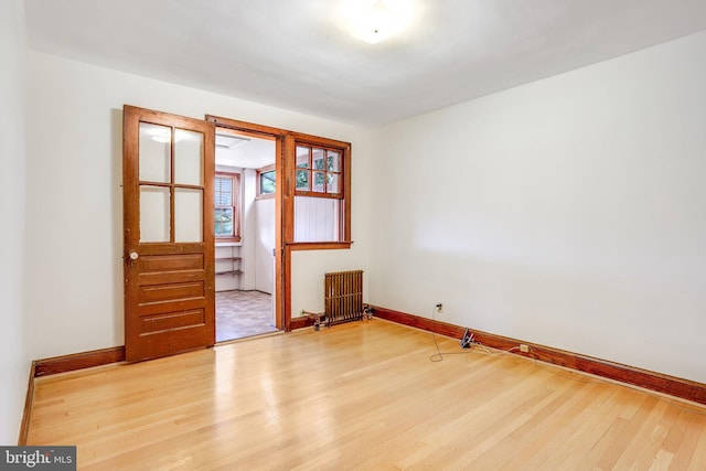 spare room with radiator, light wood finished floors, and baseboards