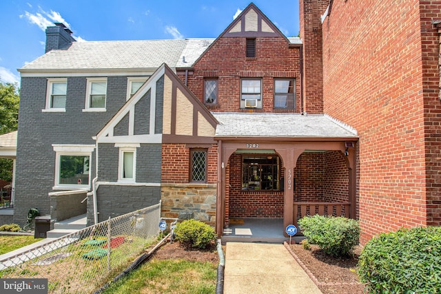 english style home with cooling unit, covered porch, brick siding, fence, and stone siding