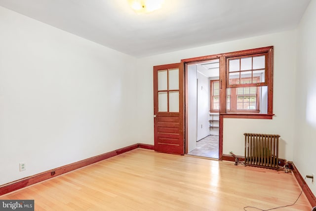 empty room with radiator heating unit, light wood-style flooring, and baseboards