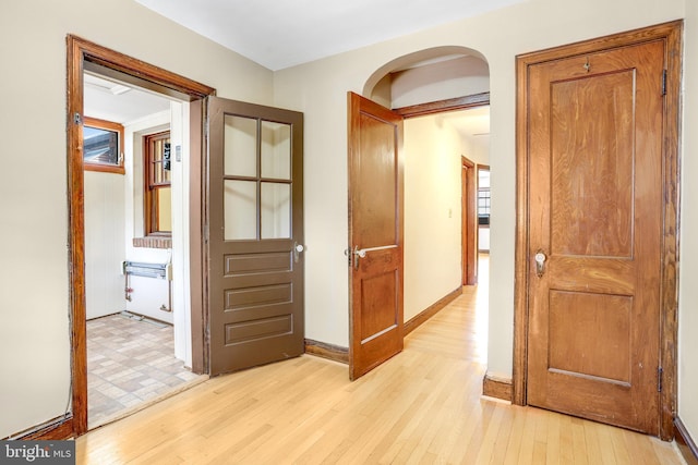 corridor with arched walkways, baseboards, and light wood-style floors