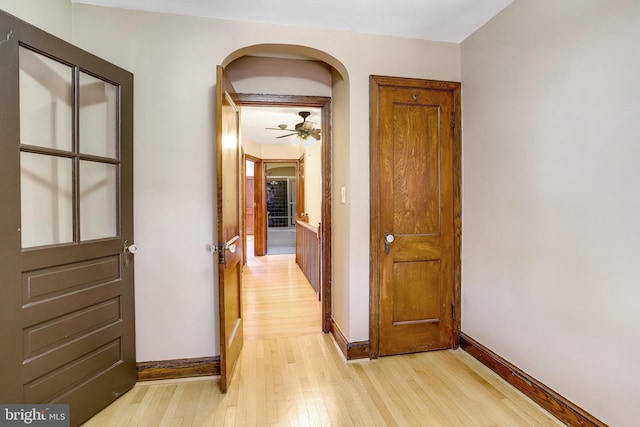 hallway with light wood-type flooring, arched walkways, and baseboards