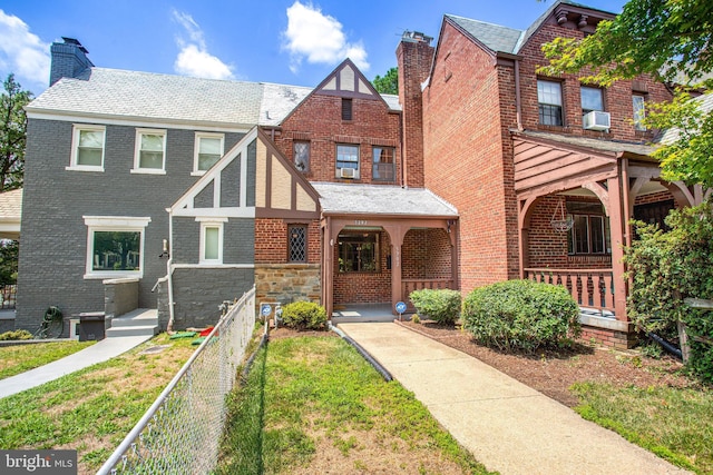 view of front of house with stone siding, a chimney, covered porch, fence, and brick siding