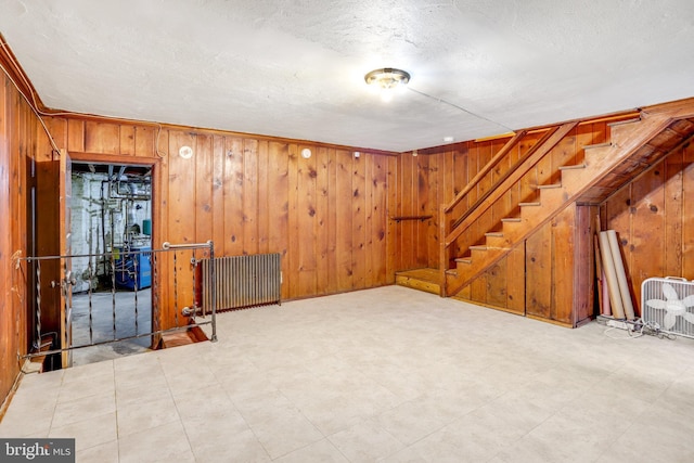 finished basement with radiator, wood walls, stairway, and tile patterned floors