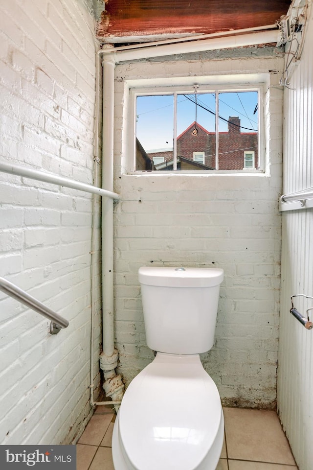 bathroom with brick wall, toilet, and tile patterned floors