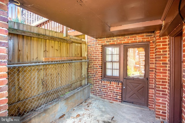 view of exterior entry with fence and brick siding