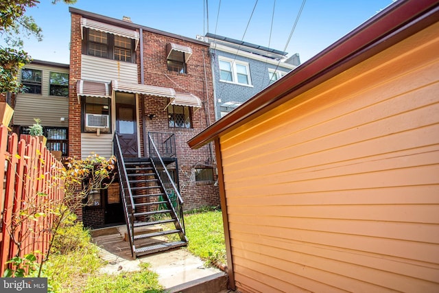 back of property with cooling unit, brick siding, fence, and stairway