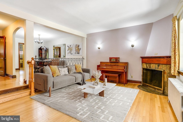 living room featuring arched walkways, radiator heating unit, wood-type flooring, a fireplace with flush hearth, and an inviting chandelier