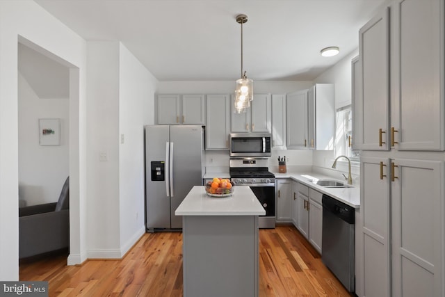 kitchen featuring light wood finished floors, a kitchen island, gray cabinets, appliances with stainless steel finishes, and a sink