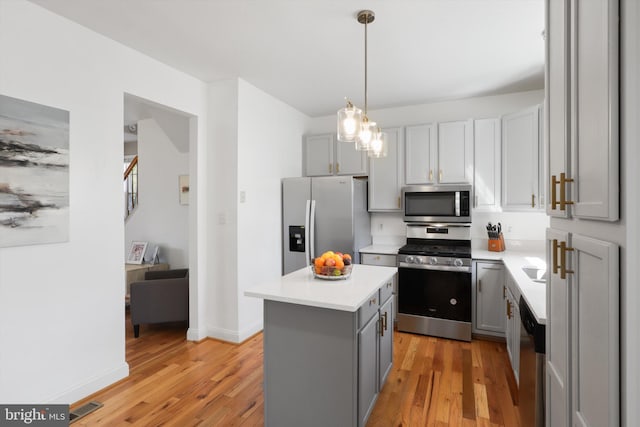 kitchen featuring gray cabinetry, a kitchen island, stainless steel appliances, light wood finished floors, and light countertops