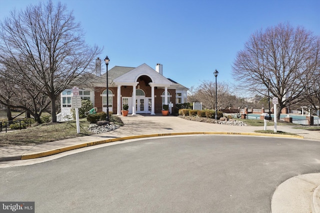 neoclassical home featuring french doors, brick siding, a chimney, and fence