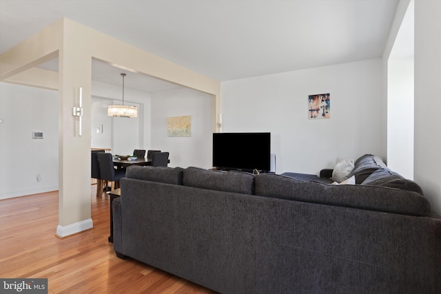 living room with baseboards, a chandelier, and light wood finished floors