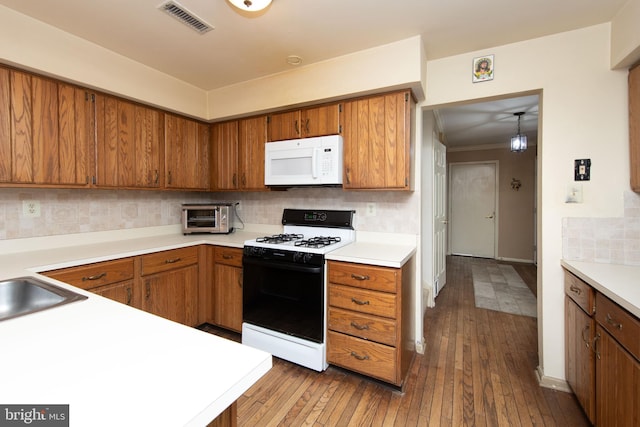 kitchen with white microwave, light countertops, brown cabinets, decorative backsplash, and gas range oven