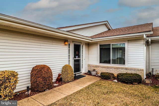 property entrance featuring a yard, a shingled roof, and brick siding