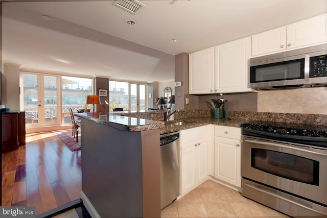 kitchen featuring stainless steel appliances, white cabinets, a sink, dark stone counters, and a peninsula