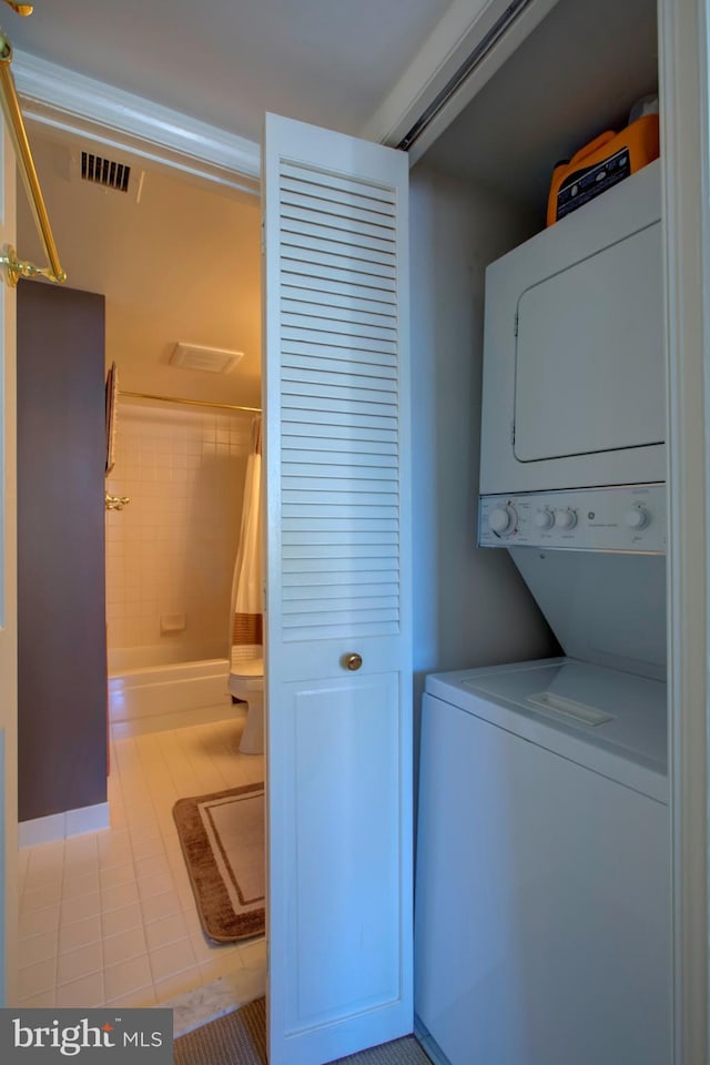 washroom featuring stacked washer / drying machine, laundry area, visible vents, and tile patterned floors