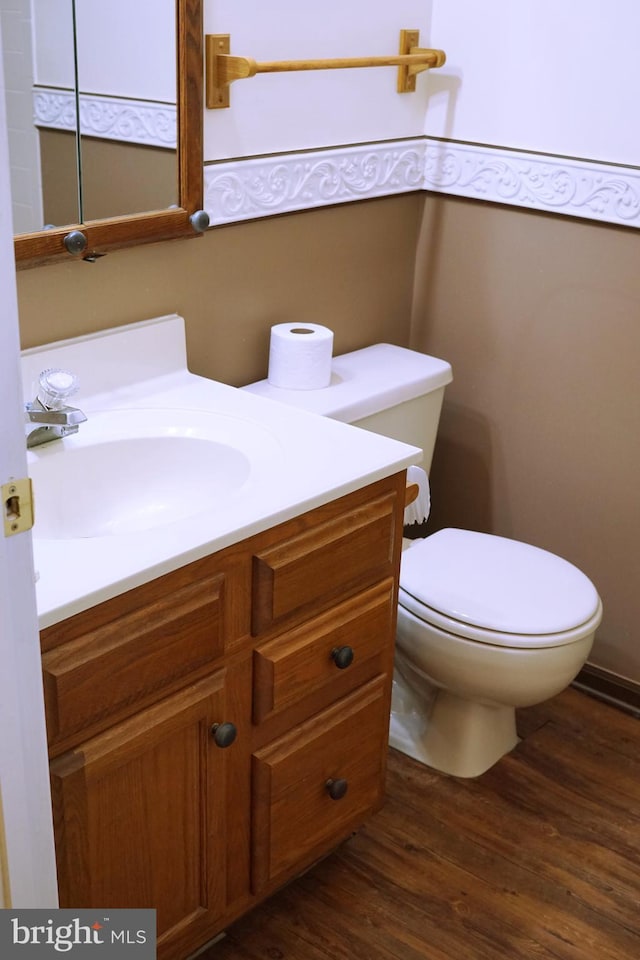 half bath with toilet, wood finished floors, and vanity