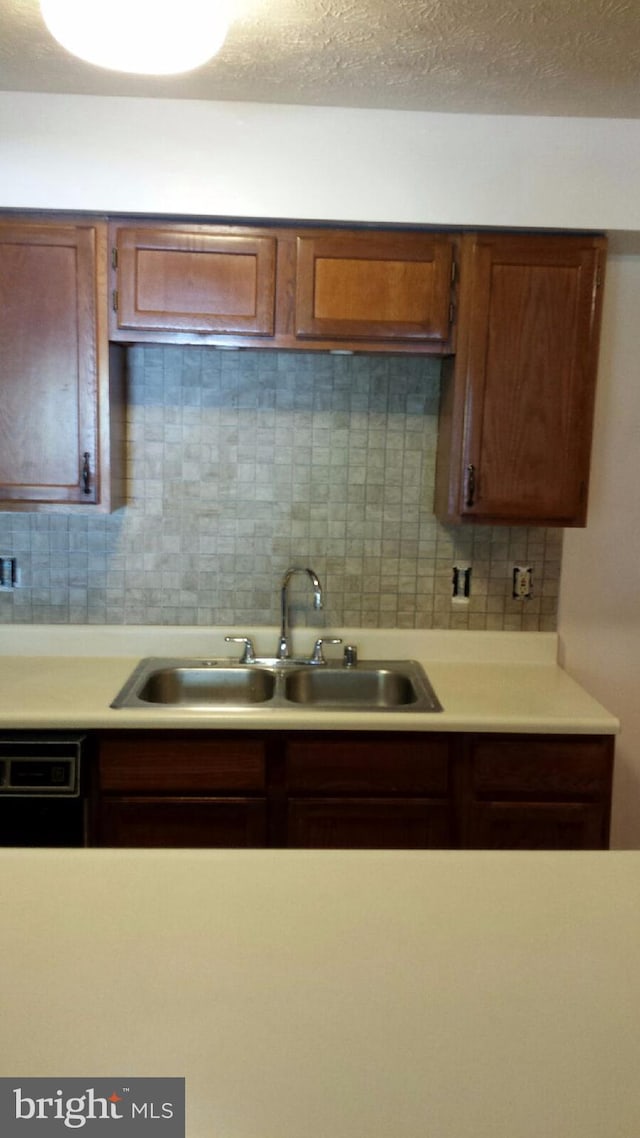 kitchen with light countertops, a sink, backsplash, and a textured ceiling