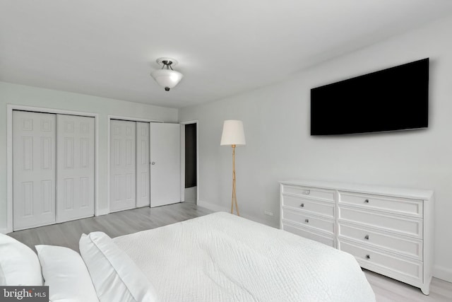 bedroom with baseboards, light wood finished floors, and two closets