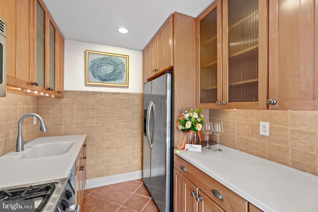 kitchen featuring brown cabinets, stainless steel appliances, light countertops, a sink, and dark tile patterned flooring