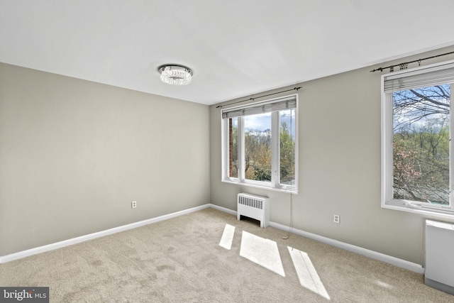 carpeted spare room featuring radiator heating unit, a wealth of natural light, and baseboards