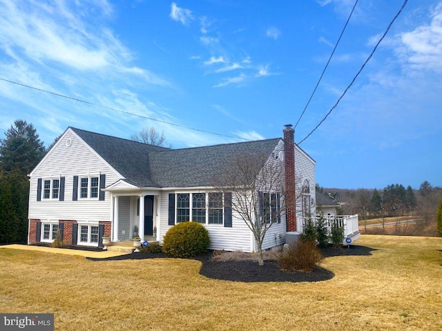 split level home featuring a front lawn, a chimney, a shingled roof, and brick siding