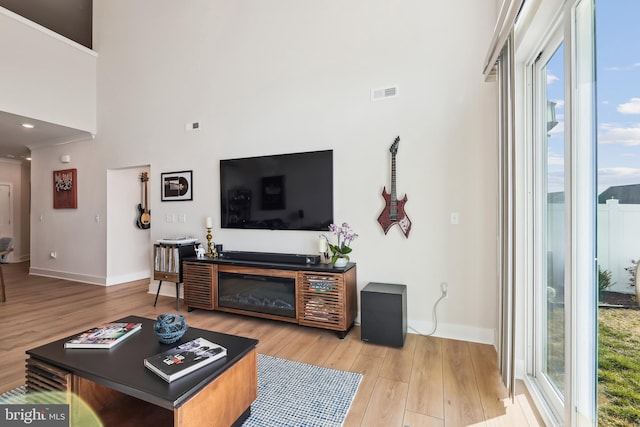 living room featuring light wood finished floors, visible vents, baseboards, and a glass covered fireplace