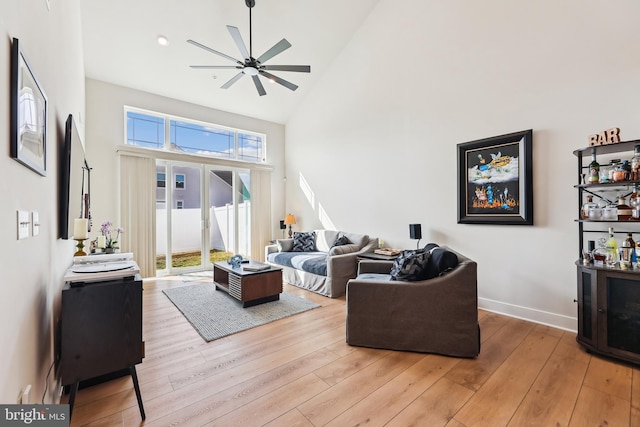 living area featuring ceiling fan, light wood-style flooring, baseboards, and high vaulted ceiling