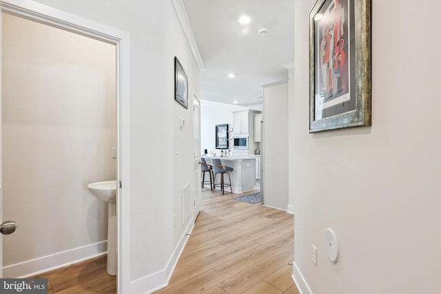 hallway featuring light wood-type flooring, visible vents, a sink, recessed lighting, and baseboards