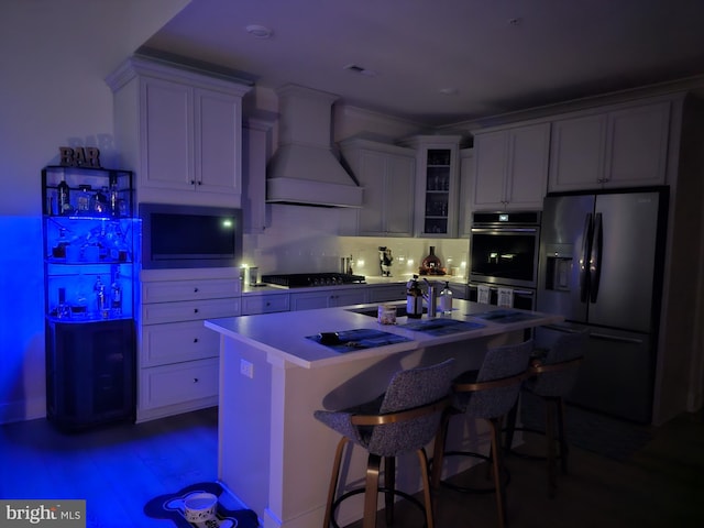 kitchen featuring a kitchen island, glass insert cabinets, double oven, refrigerator with ice dispenser, and custom exhaust hood