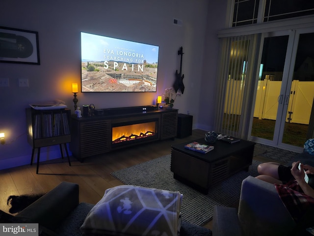 home theater with french doors, wood finished floors, visible vents, and a warm lit fireplace