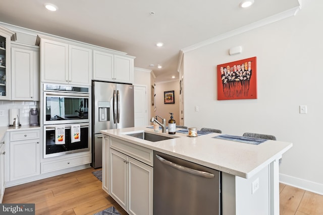 kitchen with light wood finished floors, ornamental molding, recessed lighting, appliances with stainless steel finishes, and a sink