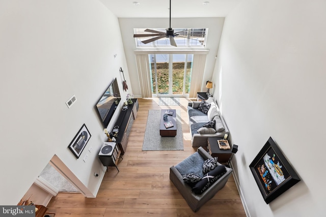 living area featuring ceiling fan, light wood-type flooring, and a towering ceiling