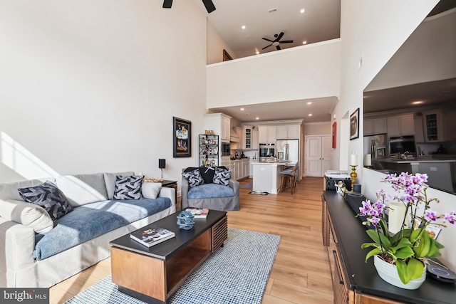 living room featuring light wood finished floors, recessed lighting, ornamental molding, ceiling fan, and a towering ceiling