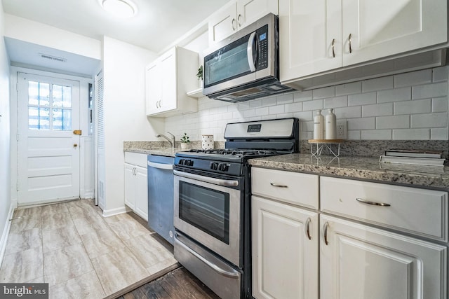 kitchen with appliances with stainless steel finishes, visible vents, white cabinetry, and tasteful backsplash