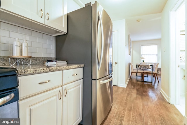 kitchen featuring baseboards, decorative backsplash, light wood-style flooring, light stone counters, and freestanding refrigerator