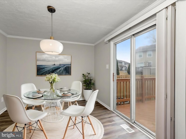 dining area with baseboards, a textured ceiling, ornamental molding, and wood finished floors