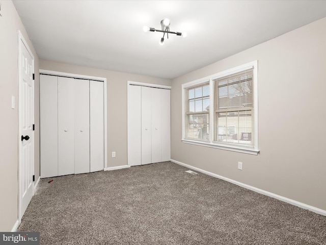 unfurnished bedroom with baseboards, carpet, visible vents, and two closets