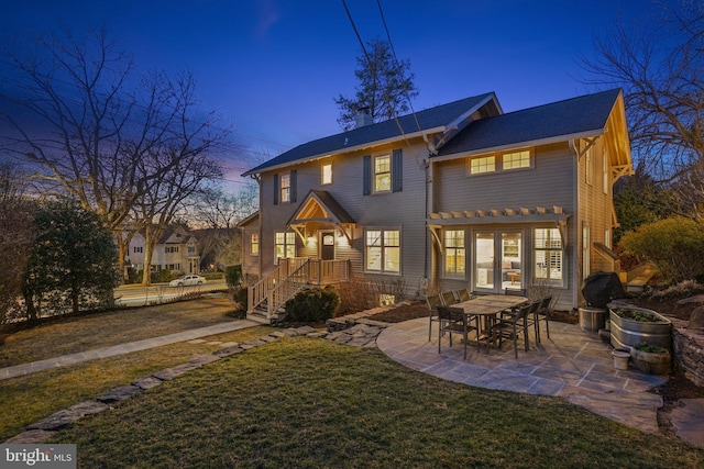 back of house at dusk with a patio, a lawn, and french doors