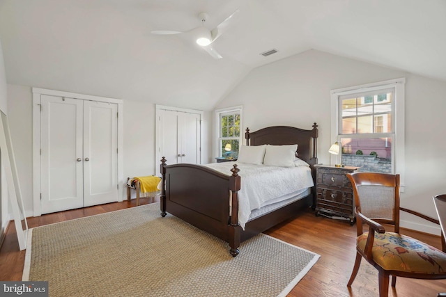 bedroom with visible vents, two closets, lofted ceiling, wood finished floors, and a ceiling fan