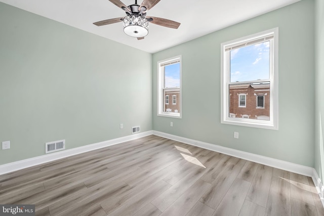 spare room featuring a ceiling fan, visible vents, light wood finished floors, and baseboards