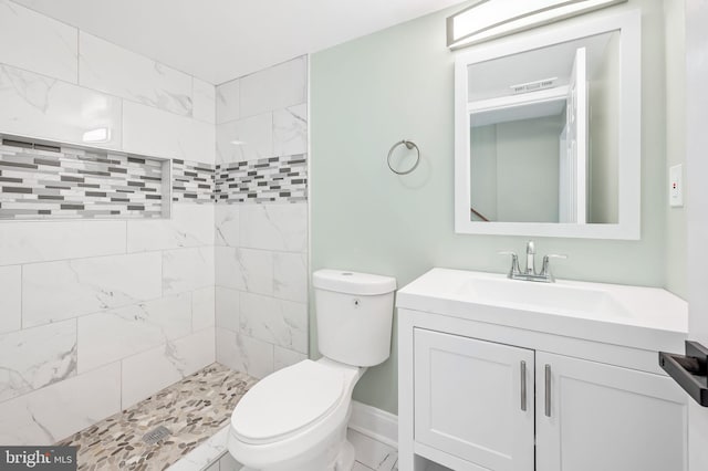 bathroom with visible vents, toilet, a tile shower, vanity, and baseboards