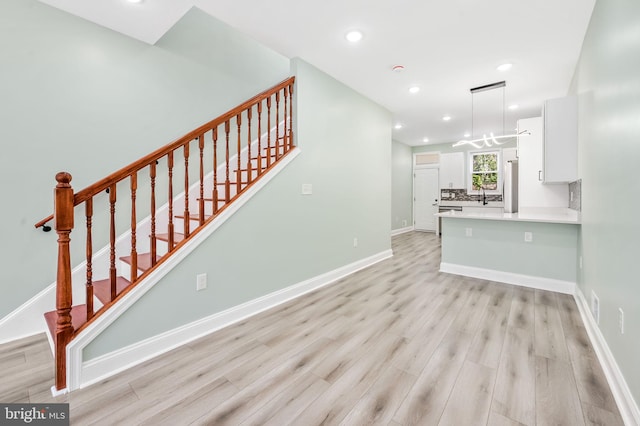 interior space featuring recessed lighting, light wood-style floors, a sink, baseboards, and stairs