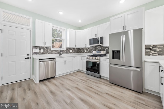 kitchen featuring stainless steel appliances, light countertops, white cabinets, a sink, and light wood-type flooring