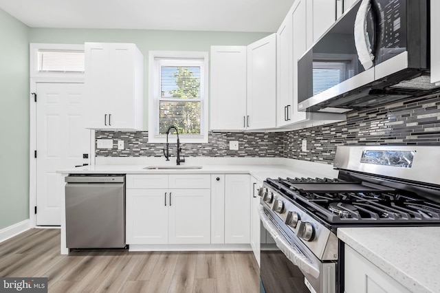 kitchen with stainless steel appliances, light wood-style floors, white cabinetry, and a sink