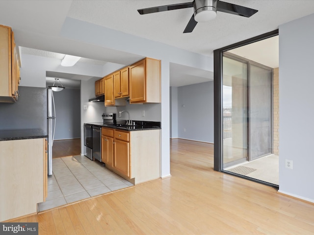 kitchen featuring dark countertops, under cabinet range hood, a wall of windows, light wood-style floors, and a sink