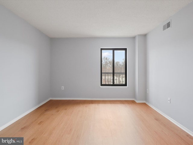 spare room featuring light wood finished floors, baseboards, visible vents, and a textured ceiling