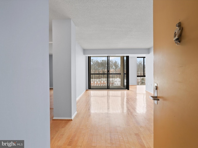 hallway with a textured ceiling, baseboards, and wood finished floors