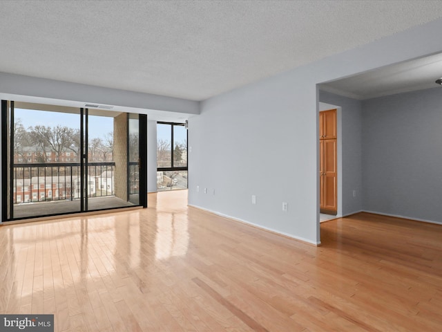 spare room featuring a textured ceiling, baseboards, and light wood-style floors